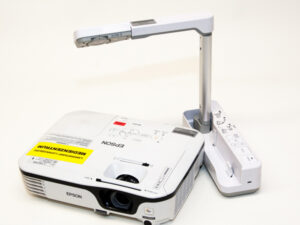 Weißer Epson-Beamer neben weißer Dokumentenkamera mit ausklappbarem Arm auf hellem Untergrund.