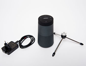 Schwarzer Bose SoundLink Revolve 2 Lautsprecher mit Netzteil und dreibeinigem Stativ auf hellem Untergrund.