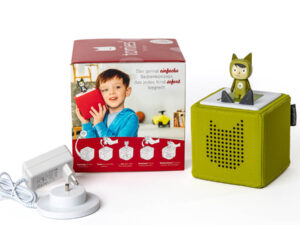 Grüne Toniebox mit Toniefigur in Katzenkostüm, weißes Ladegerät und Verpackung mit Kind und Text 'Das genial einfache Bedienkonzept, das jedes Kind sofort begreift'.