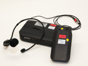 Schwarzes Shure-Headset mit Mikrofon, Funkempfänger und Sender mit Kabeln und Aufklebern.