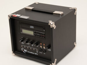 Schwarzer Würfel mit Metallverstärkungen, Bedienfeld mit Display, Drehreglern, Anschlüssen und Aufschrift 'TLS VoiceMaker MP3'.