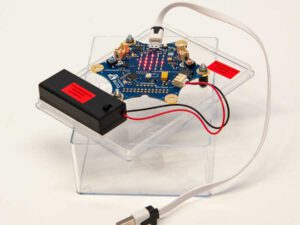 Calliope - Elektronische Schaltung mit blauem Stern-förmigem Leiterplatten-Layout, roten LED-Anzeigen, USB-Kabel und schwarzem Batteriefach auf transparentem Kunststoffständer.