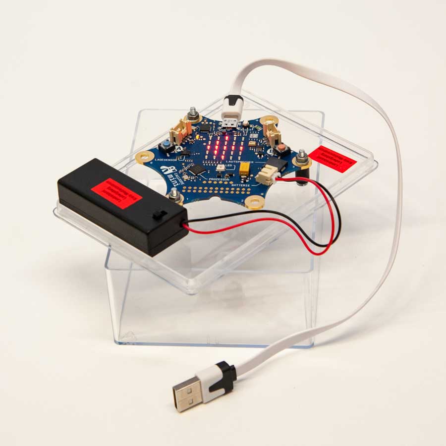 Calliope - Elektronische Schaltung mit blauem Stern-förmigem Leiterplatten-Layout, roten LED-Anzeigen, USB-Kabel und schwarzem Batteriefach auf transparentem Kunststoffständer.