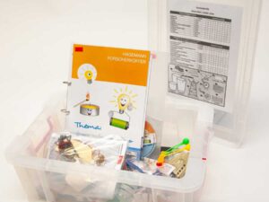 Transparenter Forscherkoffer mit Anleitung "Hagemann Forscherkoffer" und verschiedenen Experimentiermaterialien wie Batterien, Drähten und kleinen Bauteilen.
