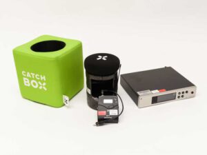 Grüner Catchbox-Würfel mit schwarzem Mikrofonaufsatz neben schwarzer Sennheiser evolution wireless G4 Verpackung mit blauem Rand und Tragegriff.