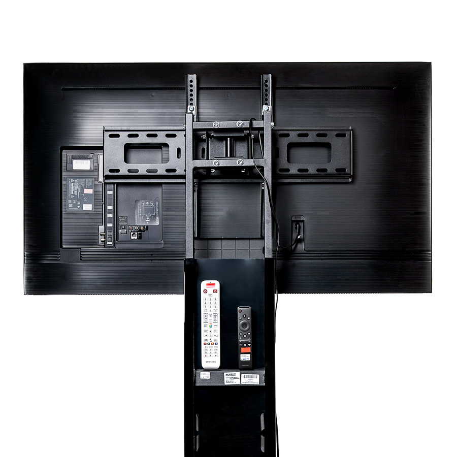 Rückseite eines großen Flachbildfernsehers mit montierter Wandhalterung und zwei Fernbedienungen auf schwarzem Ständer davor.