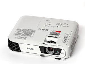 Weißer Epson-Beamer mit sichtbarer Linse und Lüftungsgitter, von oben schräg fotografiert.