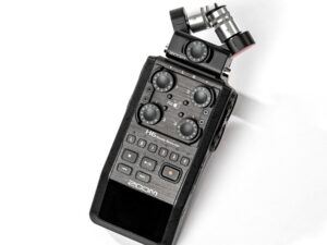 Schwarzer Zoom H6 Audiorecorder mit vier Drehreglern, mehreren Tasten und zwei Mikrofonkapseln auf weißem Untergrund.