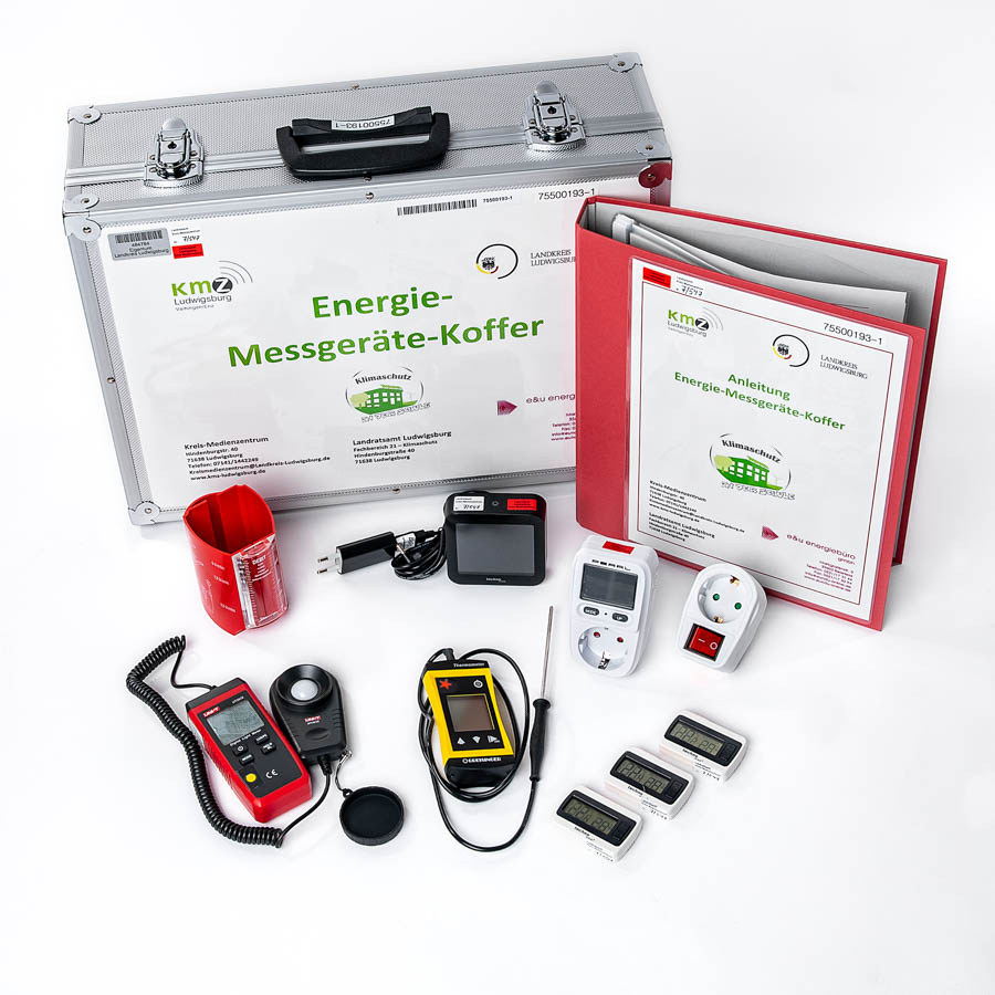 Aluminiumkoffer mit Aufschrift 'Energie-Messgeräte-Koffer', mehreren Messgeräten, Bedienungsanleitung in rotem Ordner und Zubehör auf weißem Untergrund.