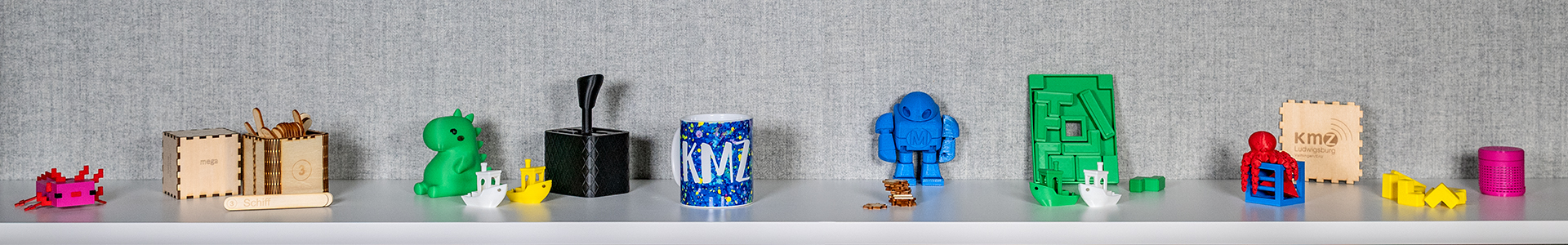 Mehrere bunte 3D-gedruckte Objekte in verschiedenen Formen und Größen auf einem weißen Regal.