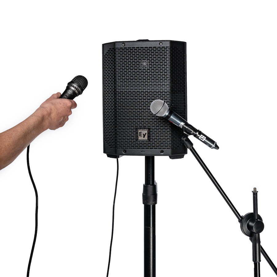 Everse Verstärkerbox auf Stativ mit zwei Mikrofonen, eines wird von einer Hand gehalten, das andere ist an einem Mikrofonständer befestigt.