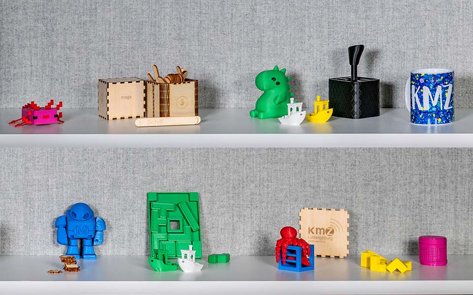 Mehrere bunte 3D-gedruckte Objekte in verschiedenen Formen und Größen auf einem weißen Regal.