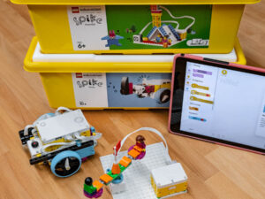 Lego-Educational-Set mit gelbem Behälter, aufgebautem Modell und Tablet mit Programmieroberfläche auf Holztisch